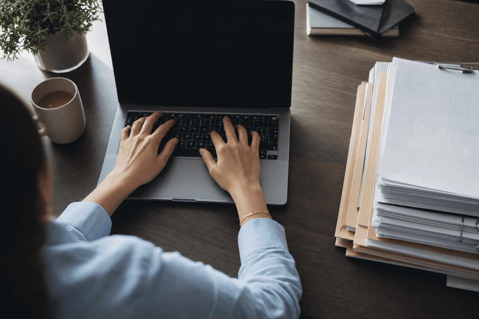 Hands typing on a laptop beside organized paperwork on a calm desk